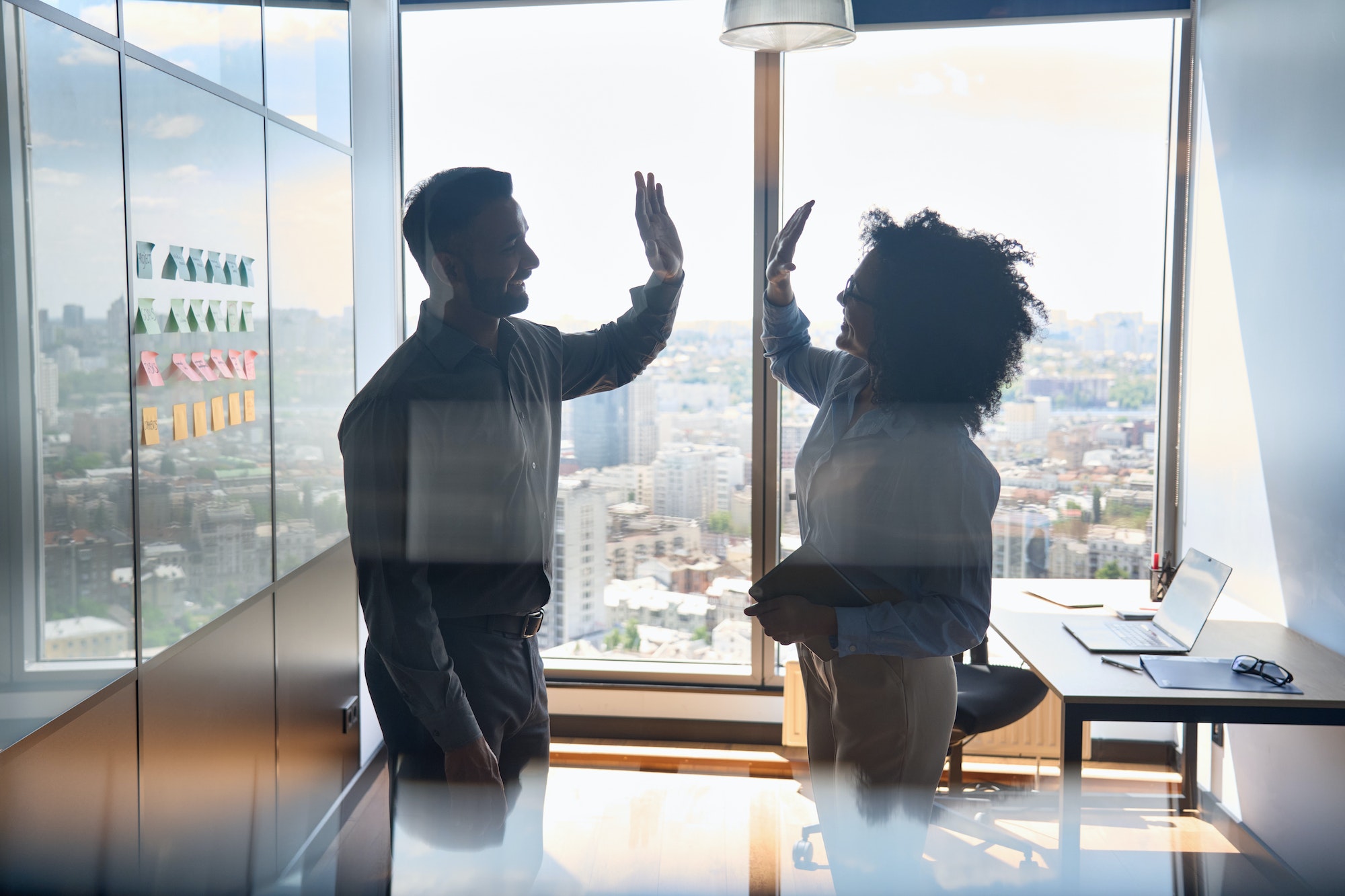 Silhouettes of multiracial business partners giving high five in office.